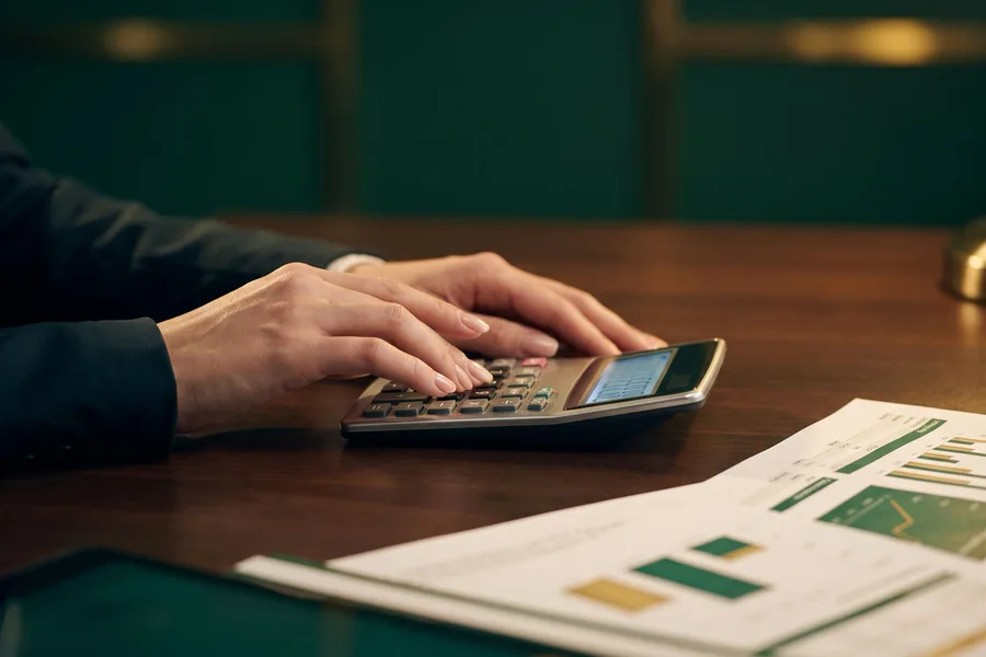 Mãos de um consultor usando calculadora ao lado de uma proposta impressa com gráficos de parcelas